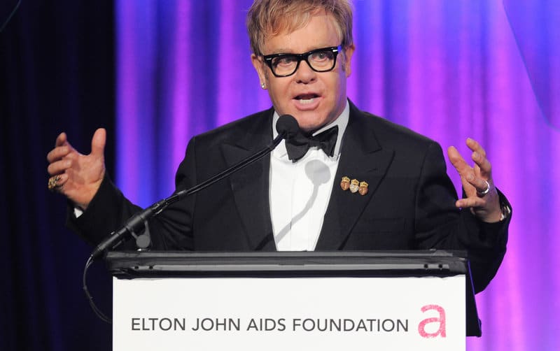 Elton John speaks to the Foundation's mission at a podium that reads 'Elton John AIDS Foundation'.