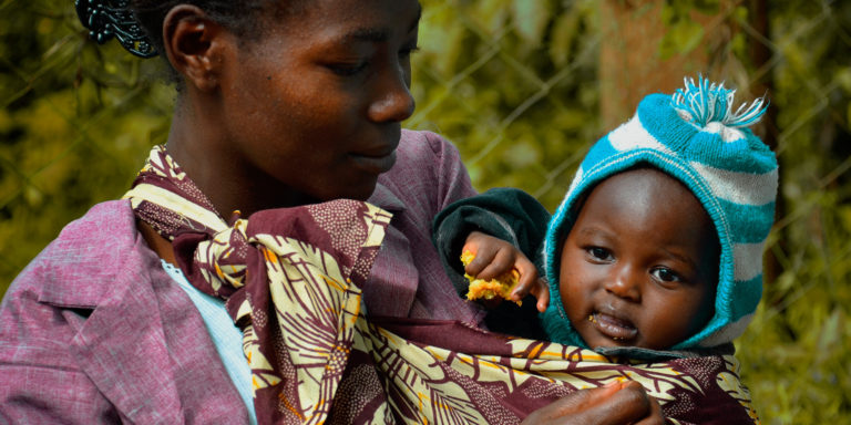 A mother who has been supported by the Elton John AIDS Foundation's work looks lovingly at her young child who she is holding.