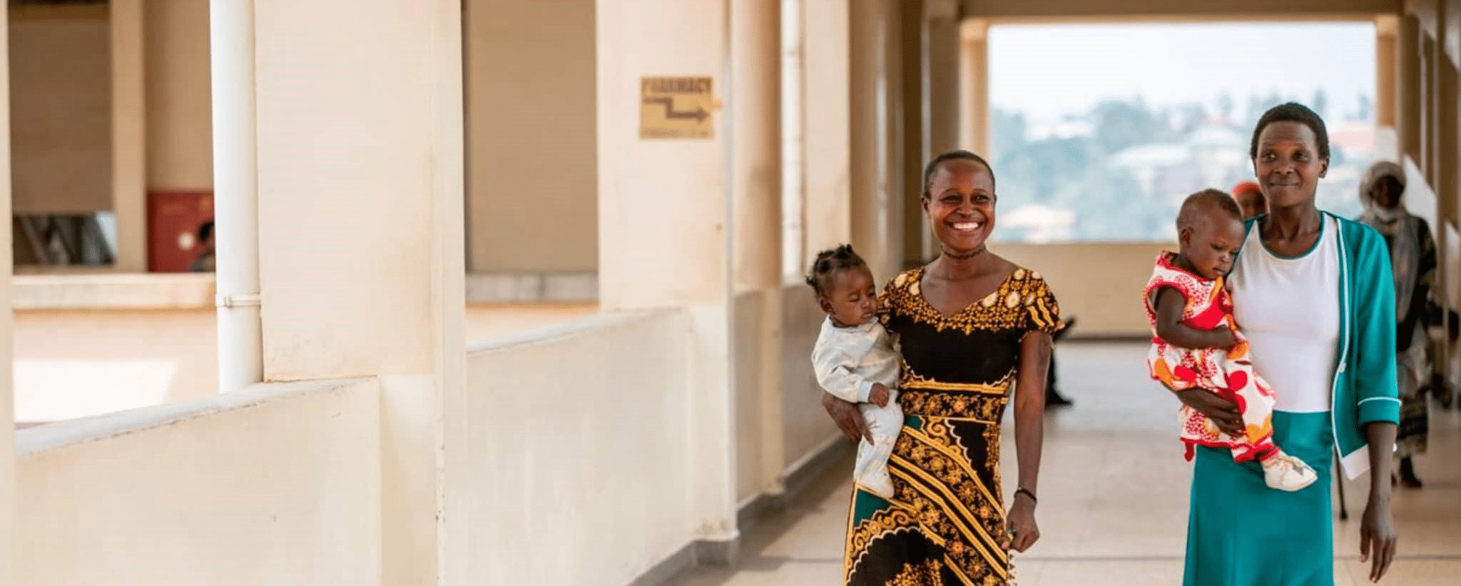 Two women walking through a corridor smiling and carrying their young children.