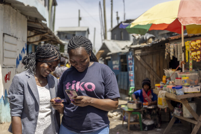 Triggerise representative in Kenya stands with a young person and is showing her how to register her account and access HIV and health care services.