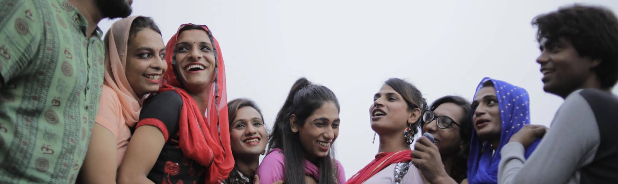 Nine program beneficiaries from India stand in a line smiling and engaging with each other.