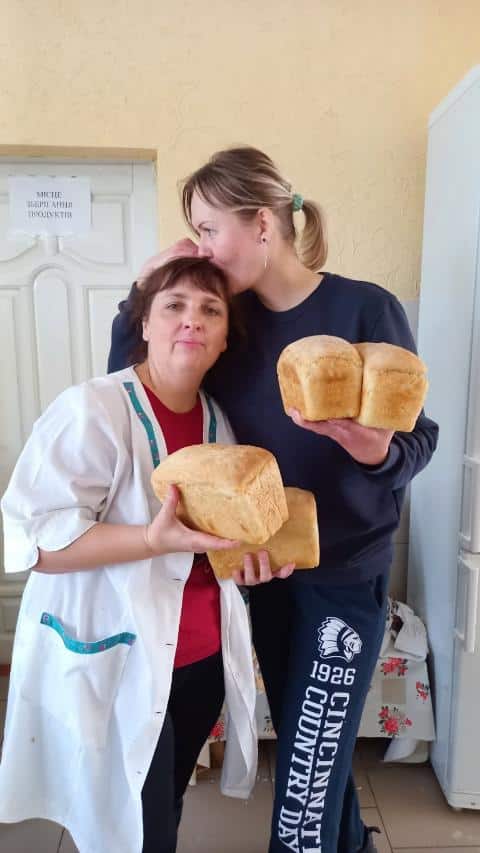 Two women stand together holding bread that they have been able to bake thanks to the support given by the Elton John AIDS Foundation.
