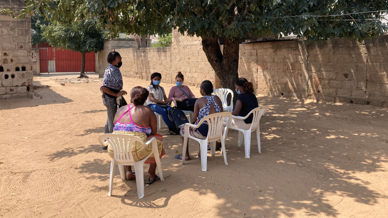 Maria, a young girl living with HIV who has been supported through partners of the Elton John AIDS Foundation, sits with her mum outside of her home speaking to peer educator from the community.