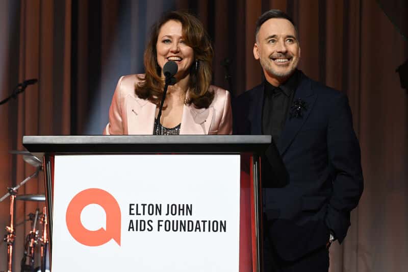 Anne Aslett and David Furnish stood behind an Elton John AIDS Foundation podium speaking to guests of the 2023 academy awards viewing party