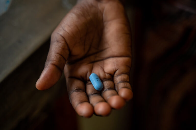 A hand holds a blue pill.