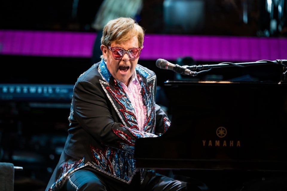Elton John performs on stage playing the piano.