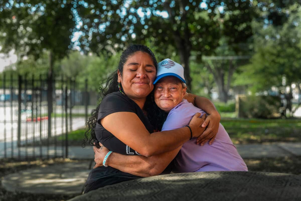 Two women embrace in a hug whilst seated.