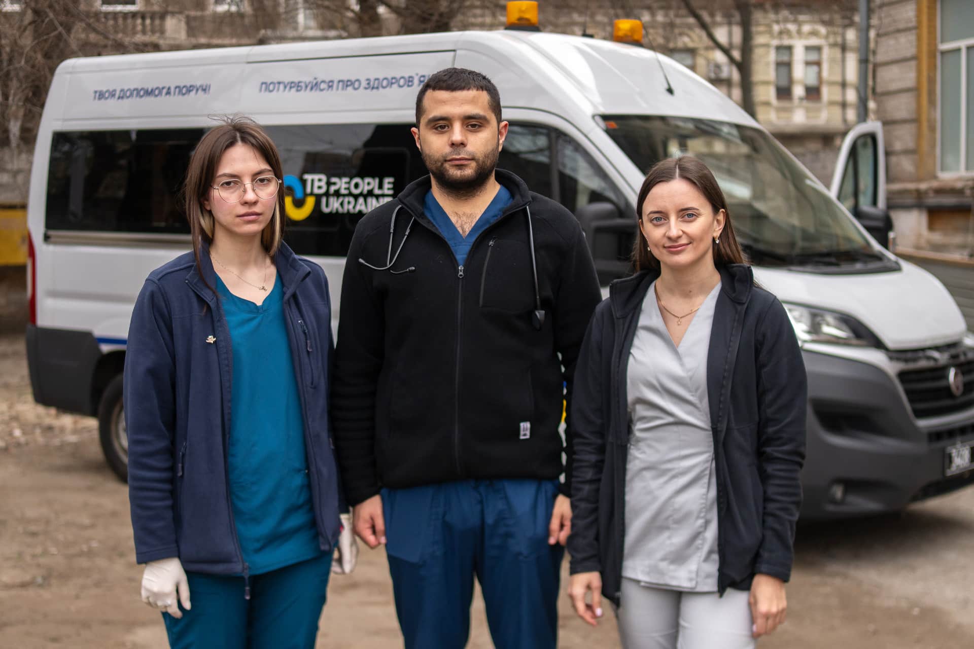 Three field doctors stand in front of TB People Ukraine mobile clinic van.