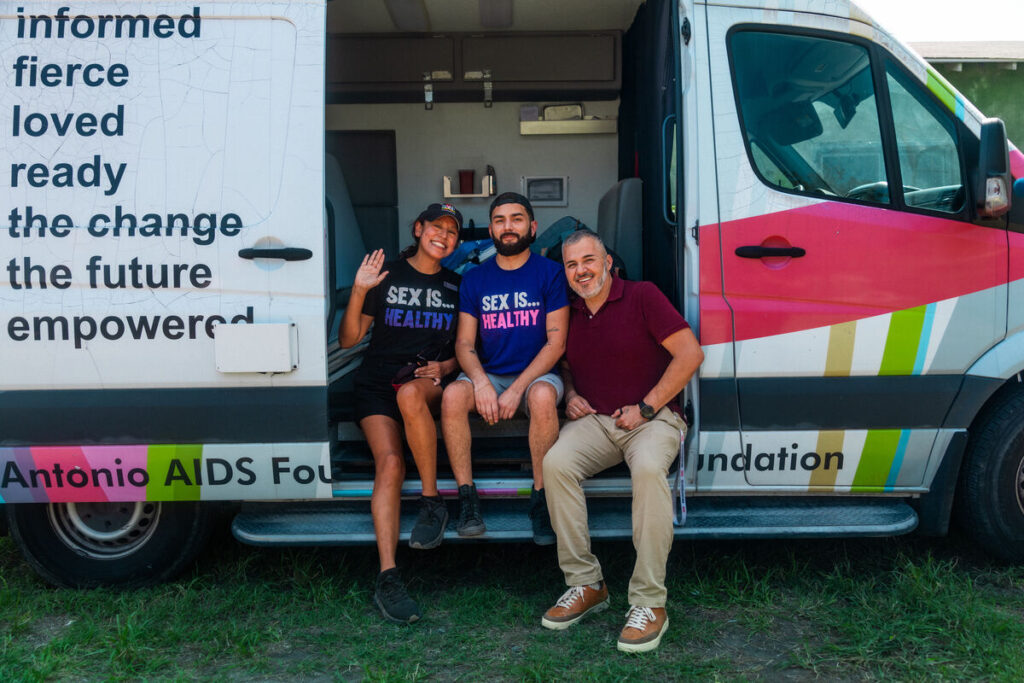 Three people sit inside the San Antonio AIDS Foundation Van smiling.