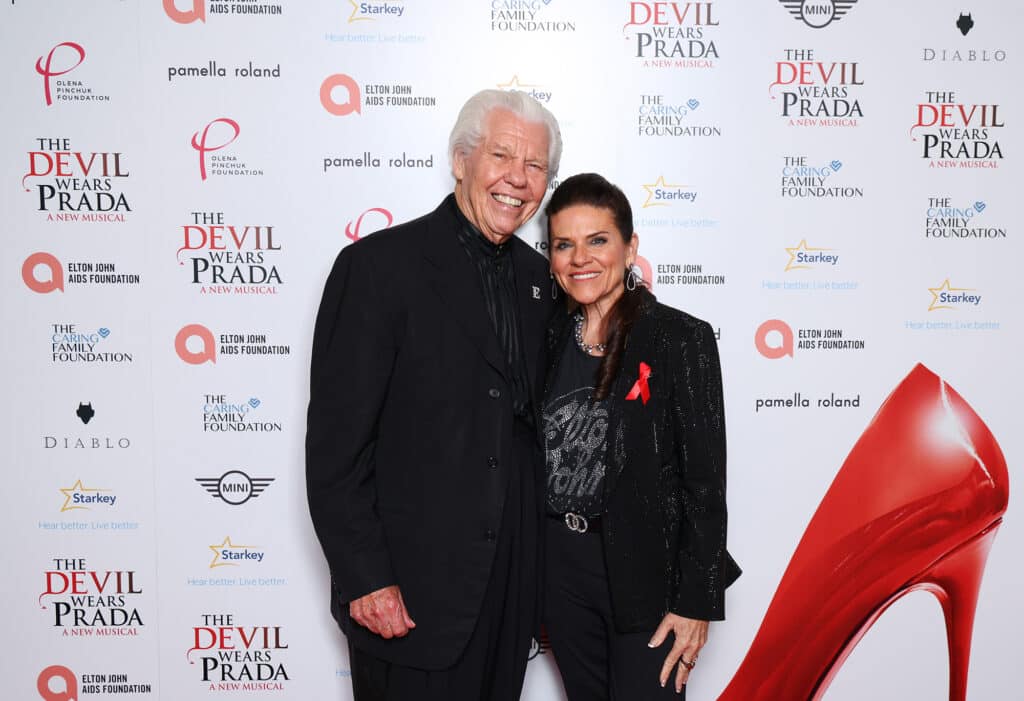 Bill and Tani Austin stand in front of the step and repeat at The Devil Wears Prada event in London.
