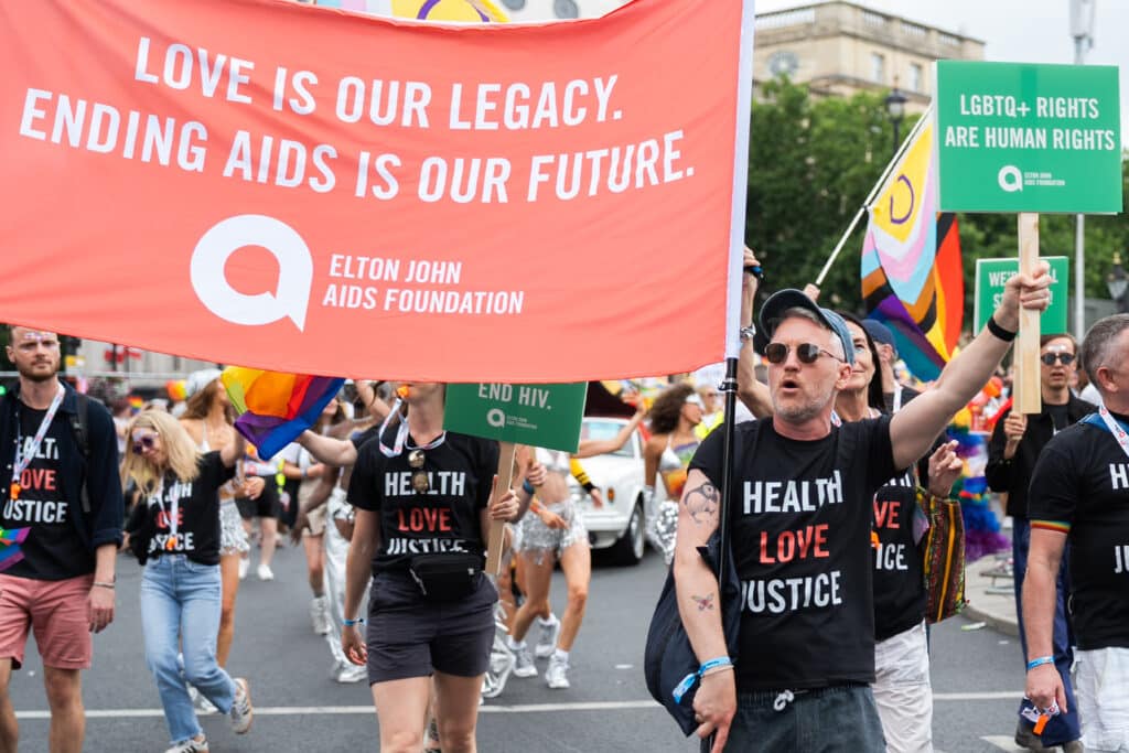 People march at London Pride. Elton John AIDS Foundation team hold large banner which reads: Love is our legacy. Ending AIDS is our future.