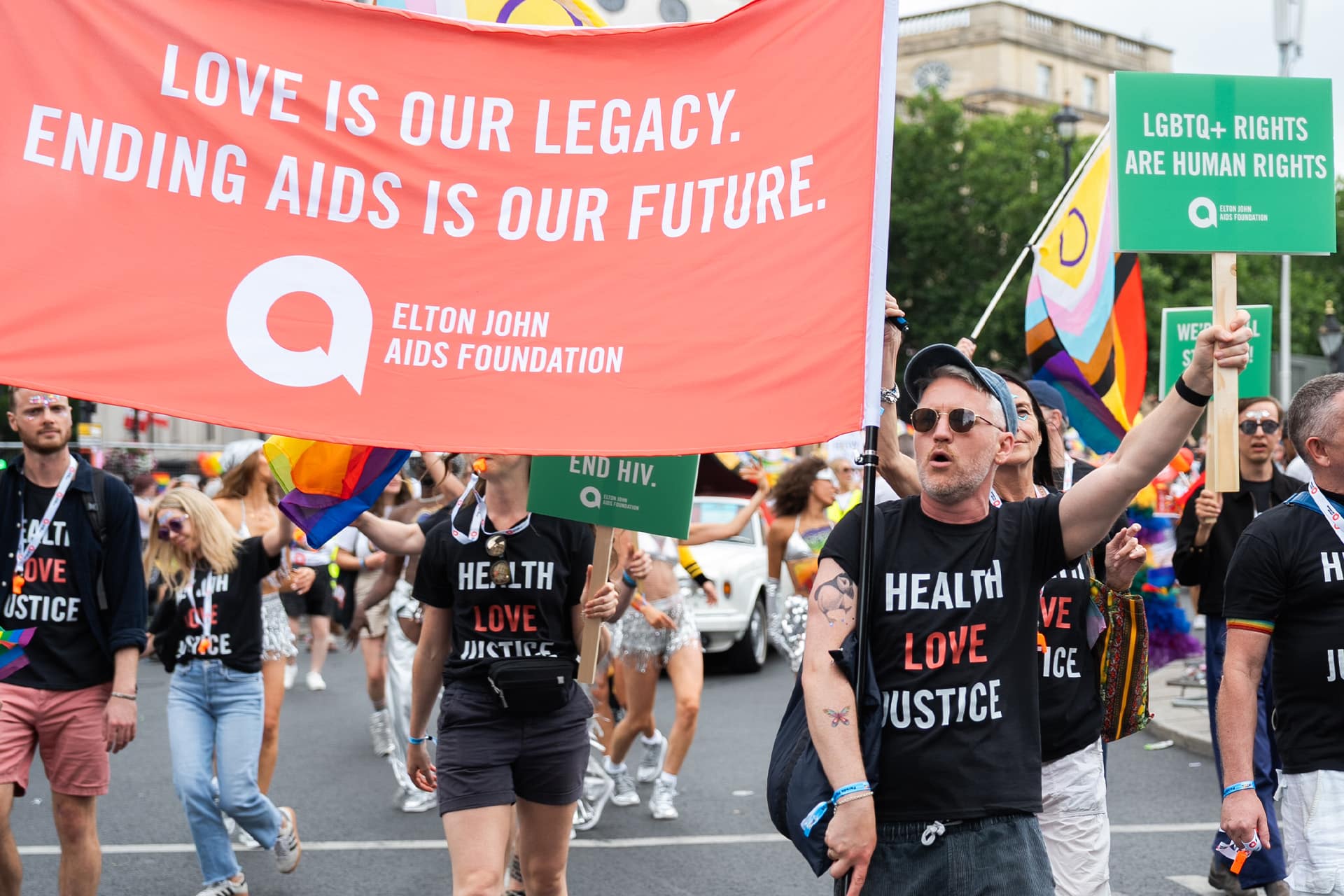 People march at London Pride. Elton John AIDS Foundation team hold large banner which reads: Love is our legacy. Ending AIDS is our future.