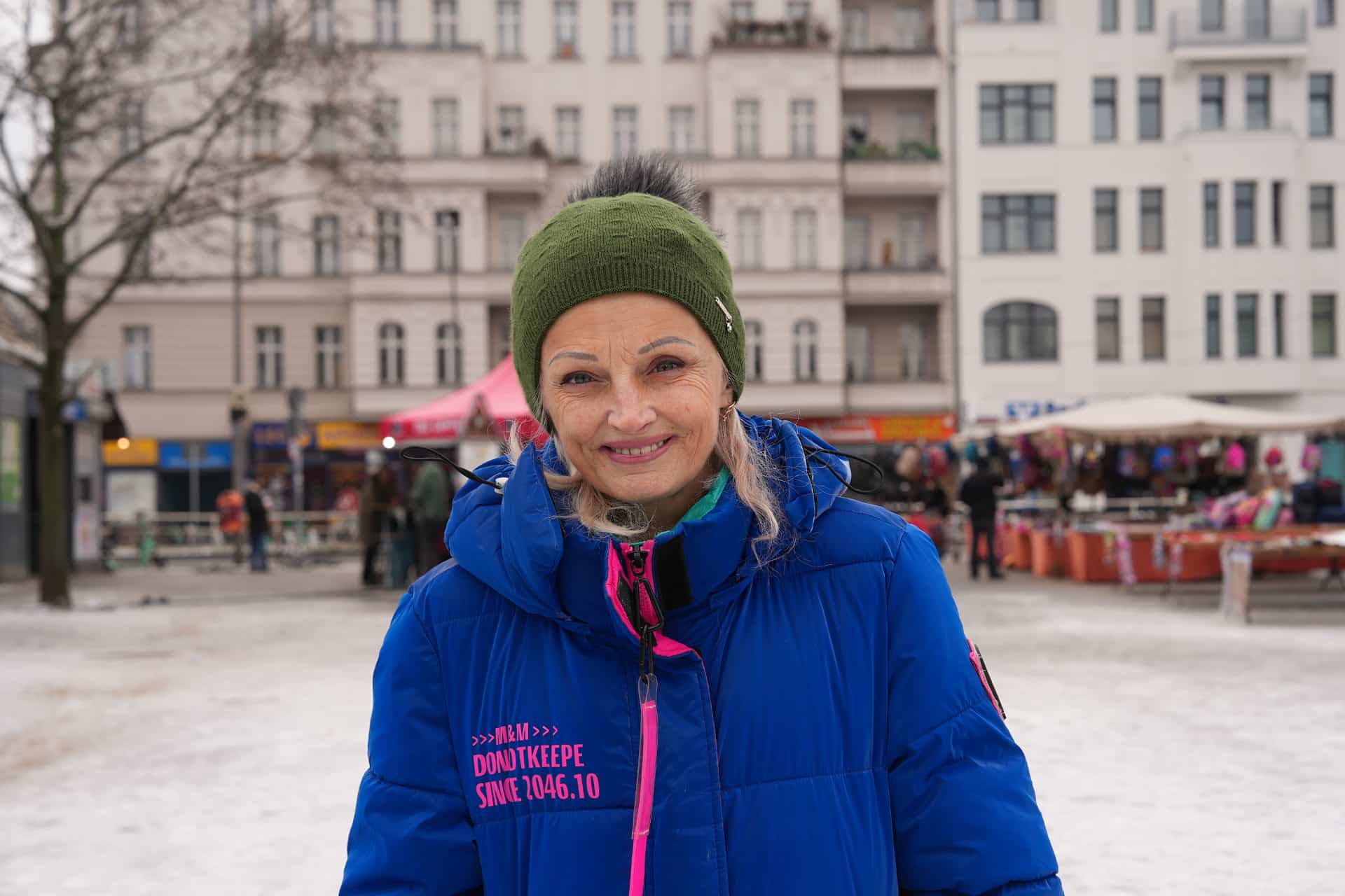 Woman smiles wearing blue puffer jacket and green bobble hat.