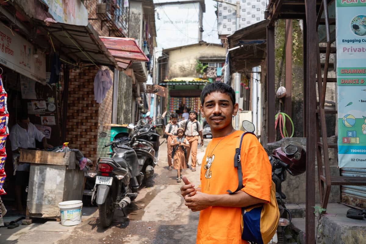 Mayur wears an orange t-shirt and stands in a narrow street.