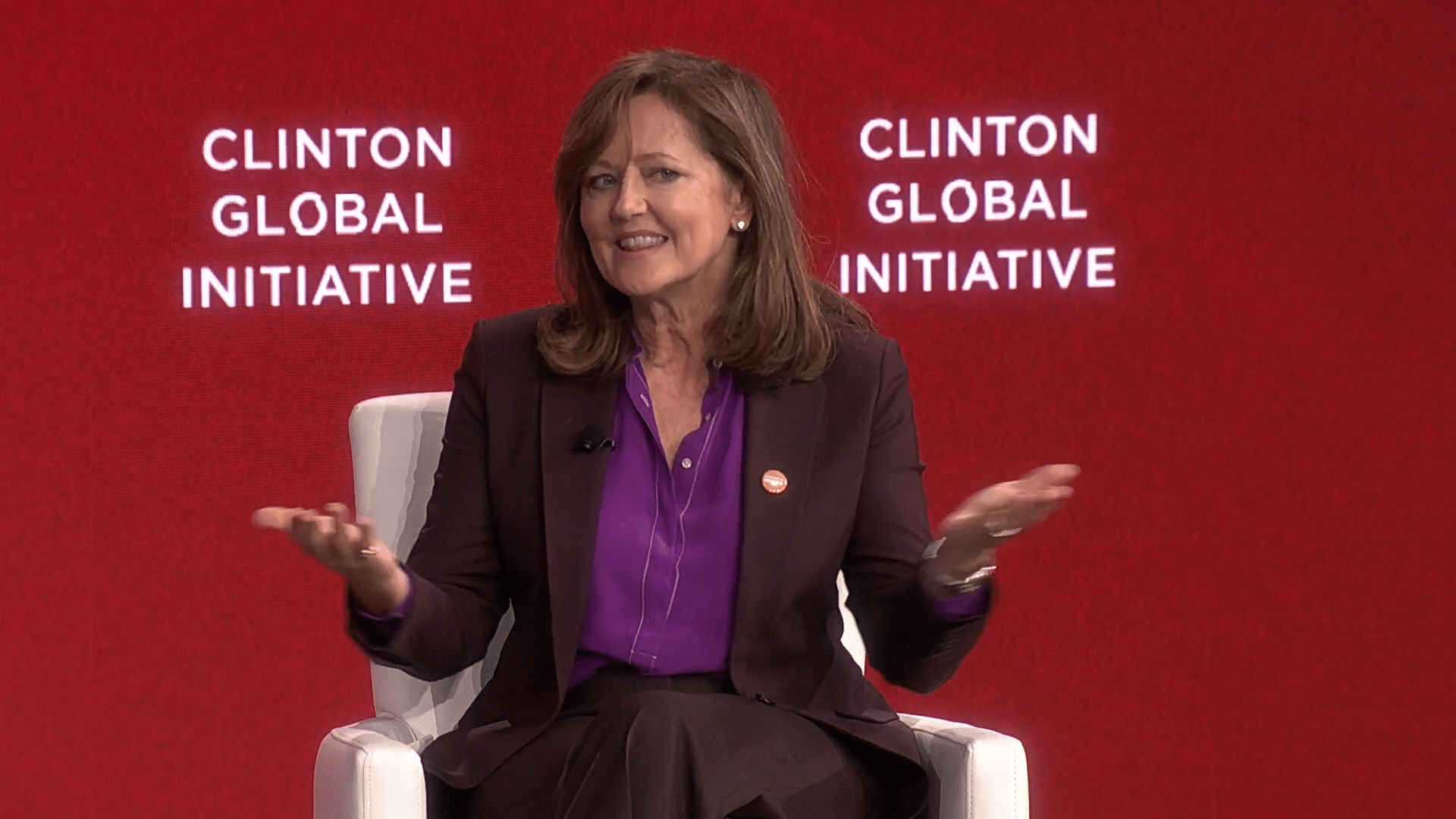 Anne Aslett sat speaking on stage. Behind her is a red background that says Clinton Global Initiative